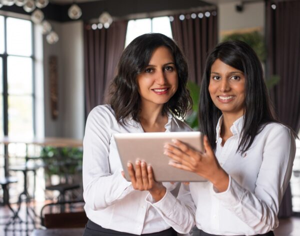 two-smiling-female-coworkers-using-tablet-computer-cafe_1262-12594