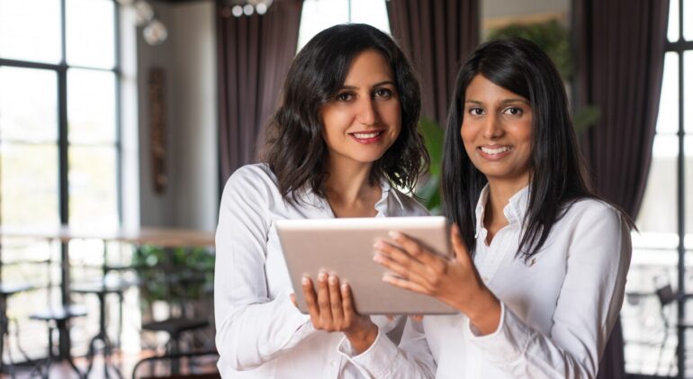 two-smiling-female-coworkers-using-tablet-computer-cafe_1262-12594