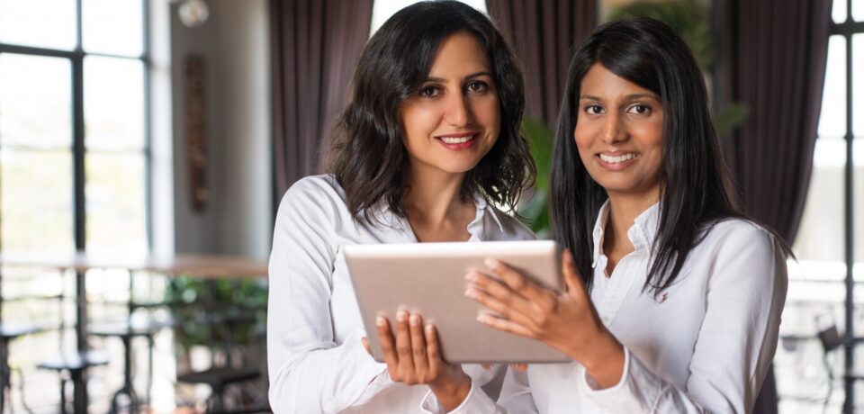 two-smiling-female-coworkers-using-tablet-computer-cafe_1262-12594